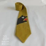 جزییات کراوات فانتزی چاپی لینن یونیسکس به رنگ زرد تیره و با طرح گربه ای که جام شراب در دست دارد، چاپ شده
