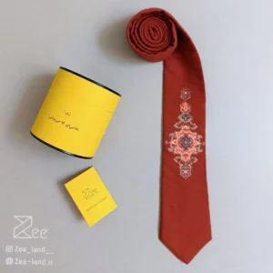کراوات سنتی قالی ۱ از جنس لینن با طرح الهام‌گرفته از نقوش اصیل فرش ایرانی روی زمینه آجری، چاپ باکیفیت، دوخت کاملاً دست‌دوز، همراه جعبه فلزی برند زی و دفترچه راهنمای نگهداری.
