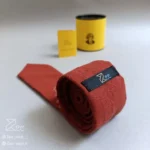 پشت کراوات سنتی قالی ۱ از جنس لینن روی زمینه آجری، با تگ برند زی، دوخت کاملاً دست‌دوز، همراه جعبه فلزی برند زی و دفترچه راهنمای نگهداری.