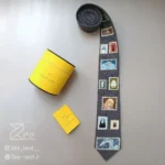 کراوات فانتزی میازاکی 1 دست‌دوز از جنس لینن با طرح تمبرهای شخصیت‌های انیمه روی زمینه طوسی، مناسب استایل کژوال و هنری با جعبه کراوات و دفترچه راهنما