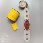 کراوات ایرانی گلیم 1 چاپ شده روی لینن کرم با طرح زرشکی و قهوه‌ای گلیم فرش ایرانی، دست‌دوز و دست‌ساز همراه جعبه استوانه فلزی برای نگهداری کراوات و دفترچه راهنمای محصول